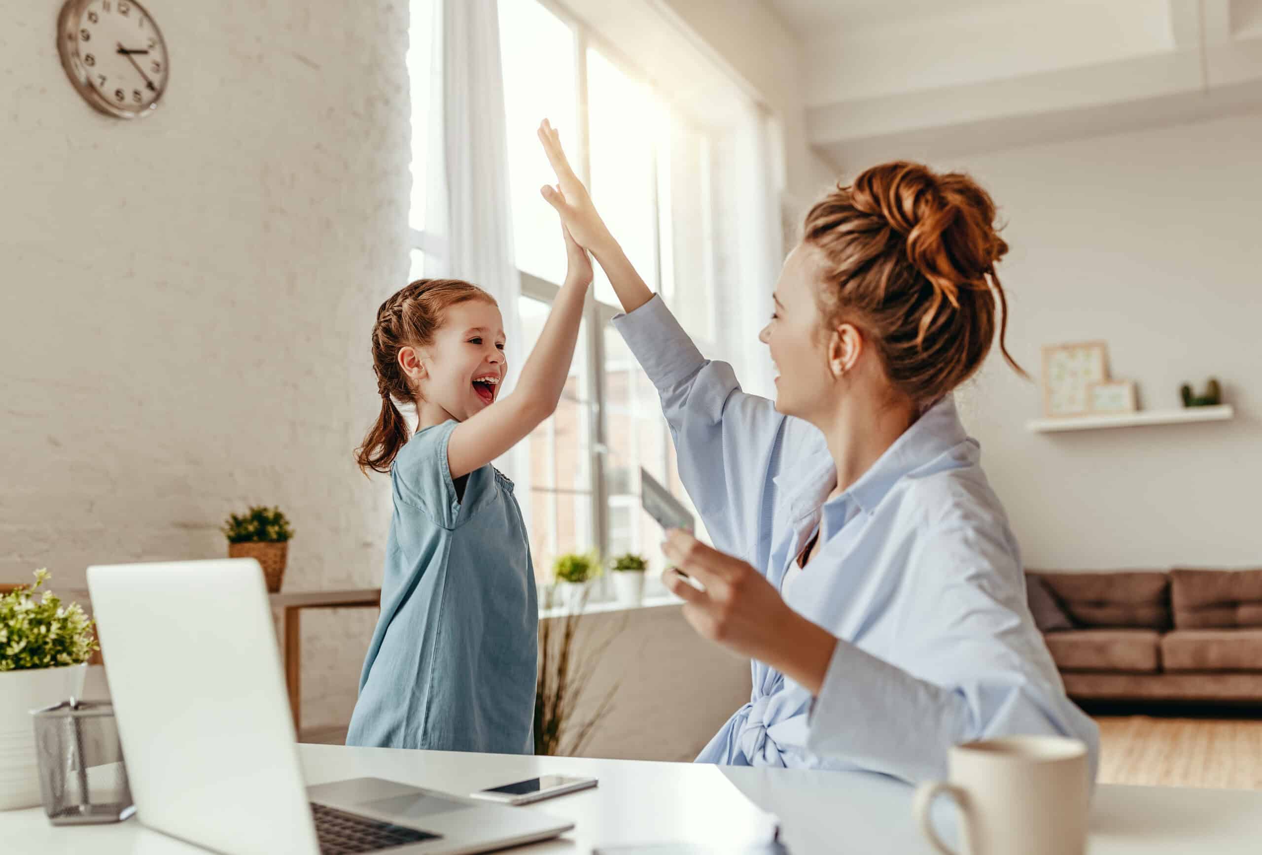 Blij kind en moeder geven een high five bij een laptop en bankpas in de hand